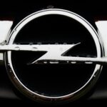 Detailed close-up shot of a wet Opel emblem with visible water droplets on the shiny silver surface.